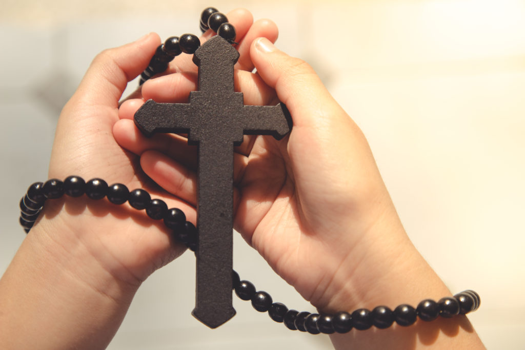 Wooden cross on praying hands with outdoor background. international prayer day.